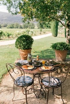 an outdoor table with chairs and plates of food on it