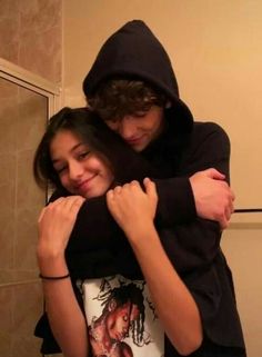 two young people hugging each other in front of a bathroom mirror and tiled wall behind them