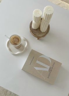 a white table topped with two candles and a cup of coffee next to a book