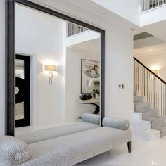 a white couch sitting in front of a mirror on top of a wooden floor next to a stair case