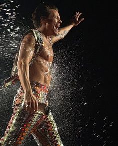 a man with no shirt on standing in the rain and spraying water all over his body