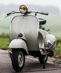 an old scooter is parked on the side of the road near some grass