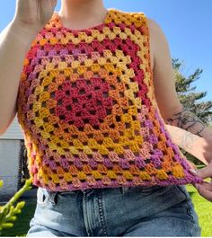 a woman wearing a colorful crocheted vest and holding a cell phone up to her ear