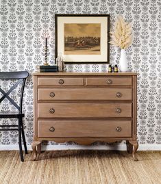 an old dresser in front of a wallpapered wall with a painting on it