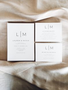 two white wedding cards sitting on top of a bed next to each other with the word l m printed on them