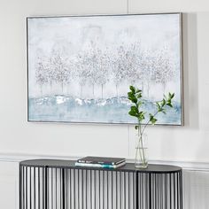 a painting hangs on the wall above a console table with a plant in front of it