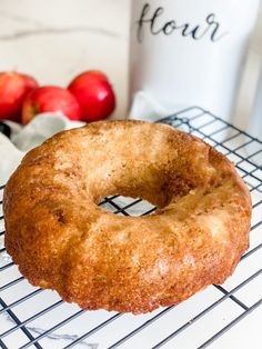 a donut sitting on top of a cooling rack next to apples and a cup