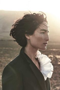 a woman in a black suit and white ruffled collar looks off into the distance