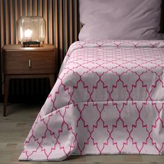 a bed with a pink and white comforter next to a night stand