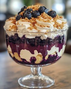 a dessert dish with blueberries, cream and crumbled toppings in a glass bowl