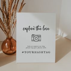 a card with the words capture the love next to a vase with dried grass in it