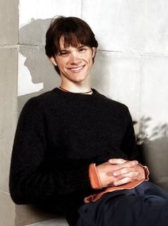 a young man sitting on the ground smiling