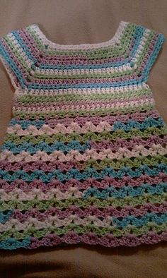 a crocheted baby dress laying on top of a bed next to a pillow