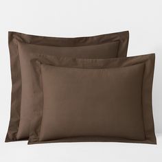 two pillows and one pillow case with brown sheets on top of each other in front of a white wall