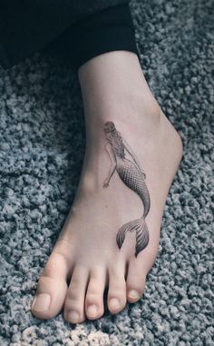 a woman's foot with a mermaid tattoo on it