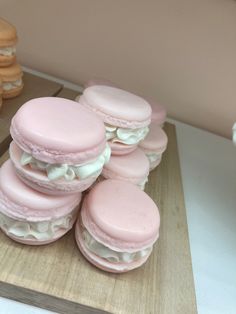 a pile of pink macaroons sitting on top of a cutting board next to some cookies