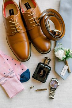 a pair of brown shoes next to a watch, tie and other items on a white surface