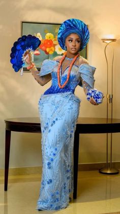 a woman in a blue dress and headdress holding a fan standing next to a table