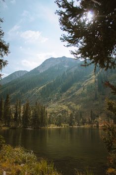 a lake surrounded by trees and mountains in the distance with sun shining on it's side