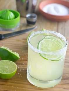 two margaritas with lime slices and sugar on the rim, sitting on a cutting board