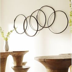 four metal circles hanging on the wall above a table and vase with flowers in it