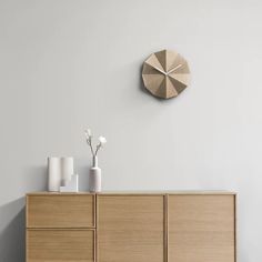 a wooden cabinet with vases and a clock on the wall above it in a white room