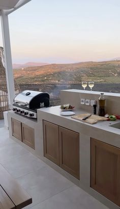 an outdoor kitchen with grill, sink and wine glass on the counter top overlooking mountains