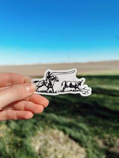 a person holding up a sticker with horses on it in the middle of a field