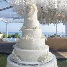 a large white wedding cake sitting on top of a lush green field next to the ocean