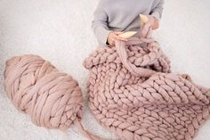 a baby sitting on top of a large blanket next to a ball of yarn and a stuffed animal