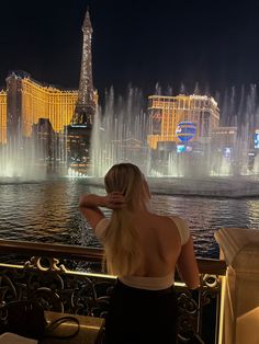 a woman is looking at the fountains in front of the las vegas hotel and casino