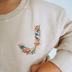 a baby wearing a sweater with the letter j on it's chest and embroidered flowers