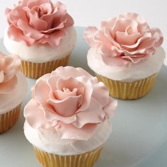 four cupcakes with pink frosting and flowers on them sitting on a plate