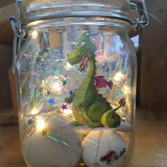 a glass jar filled with white balls and a stuffed dinosaur in the bottom, sitting on a wooden table