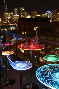 illuminated chairs and tables on a balcony overlooking the city skyline at night, lit up with colorful lights