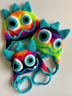 three crocheted hats with eyeballs on them sitting next to each other in the shape of monsters