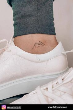 a woman's ankle with a small mountain tattoo on her left side ribcage