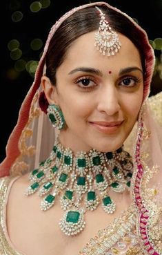 a woman in a bridal outfit with green and pink jewelry on her head, smiling at the camera