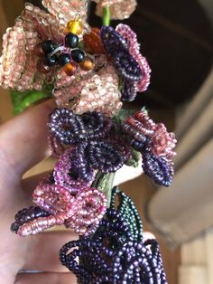 a person holding some beads and flowers in their hand with the bead work on them