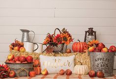 a table topped with buckets filled with apples and pumpkins next to other fall decorations