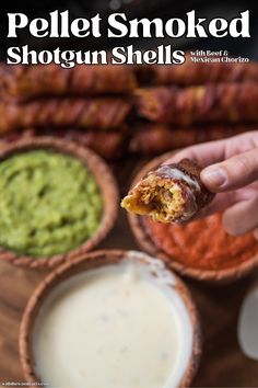 a person holding up a piece of food in front of some bowls and dips