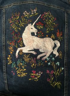 an embroidered unicorn is on the back of a jean jacket with flowers and leaves around it