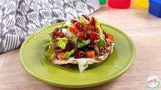 a green plate topped with an open faced sandwich covered in lettuce and tomatoes