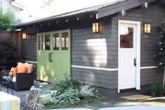 a small gray shed with green doors and windows on the side, sitting next to a patio