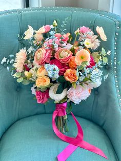 a bouquet of flowers sitting on top of a blue chair next to a pink ribbon