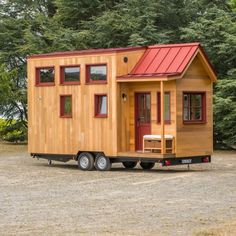 a tiny house on wheels is parked in front of some trees and grass with a red roof