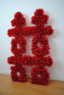 a large red sculpture sitting on top of a wooden floor next to a white wall