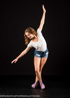 a young woman is dancing on stage with her arms in the air and one leg up