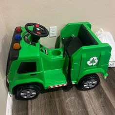 a green toy truck sitting on top of a wooden floor next to a white wall