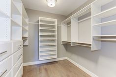 an empty walk in closet with white shelving and wood flooring on the side